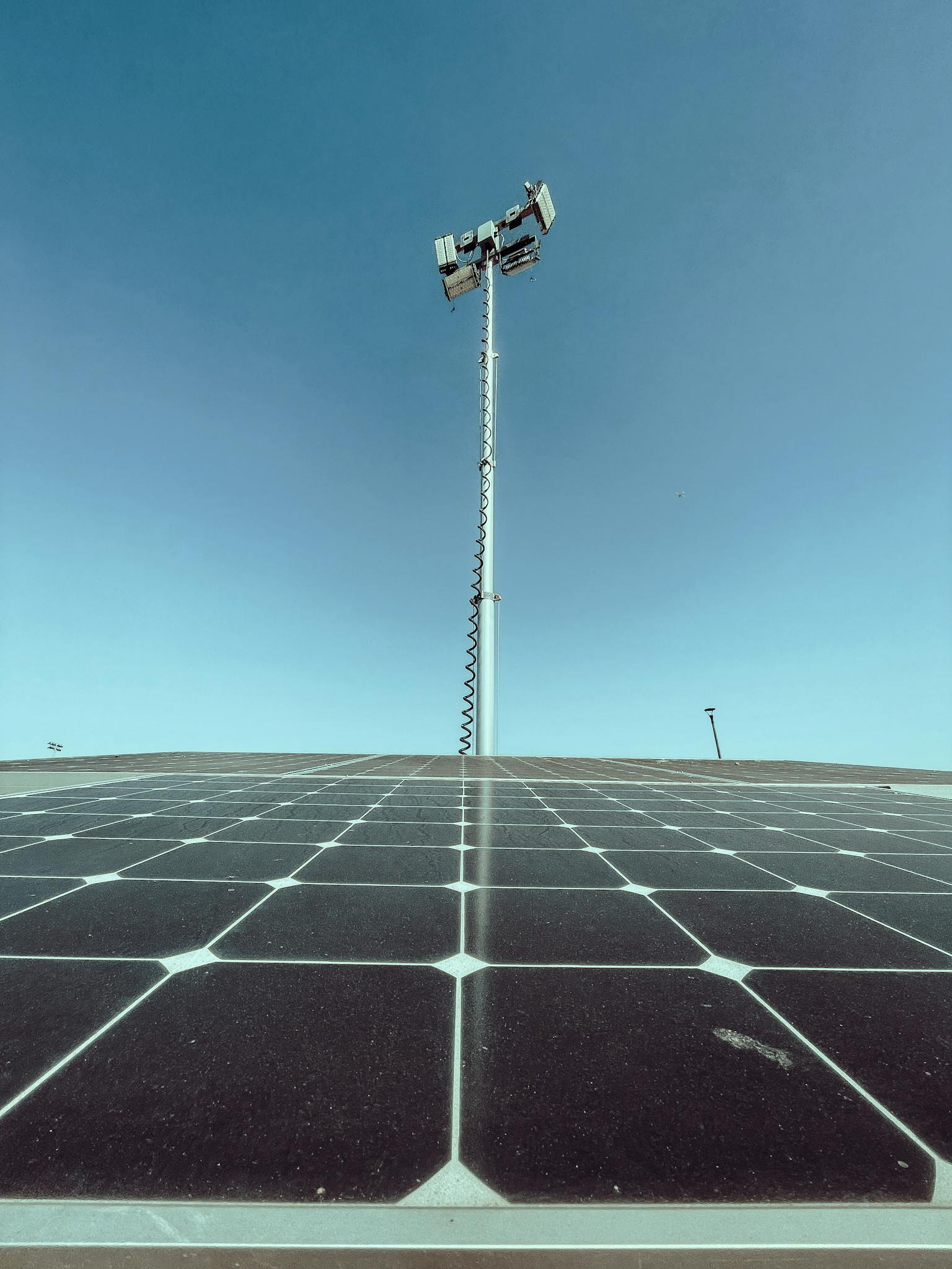 Solar panels under a clear blue sky with a communication tower in the background.
